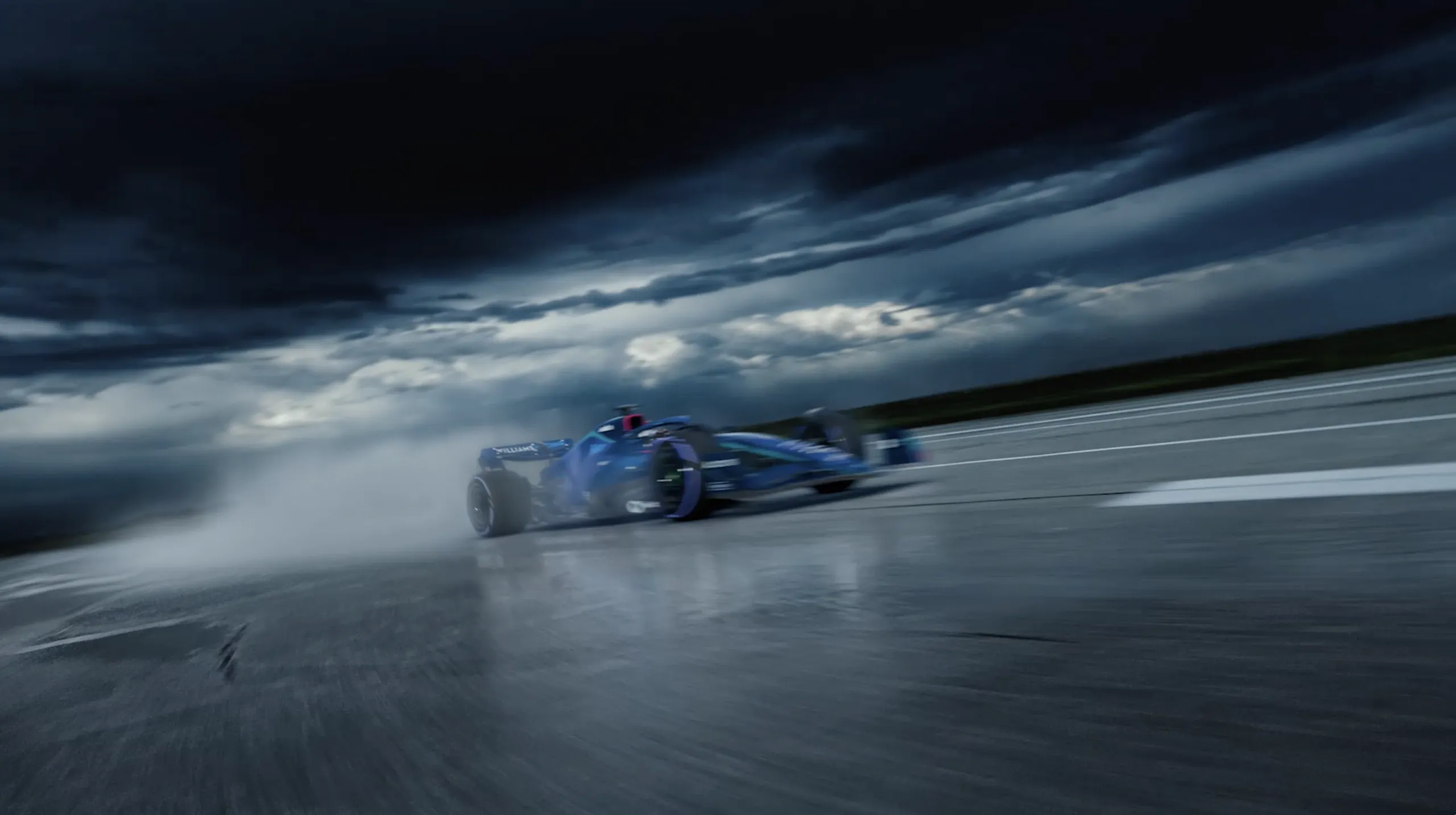 Williams Racing car tearing through spray on a wet track under a stormy sky
