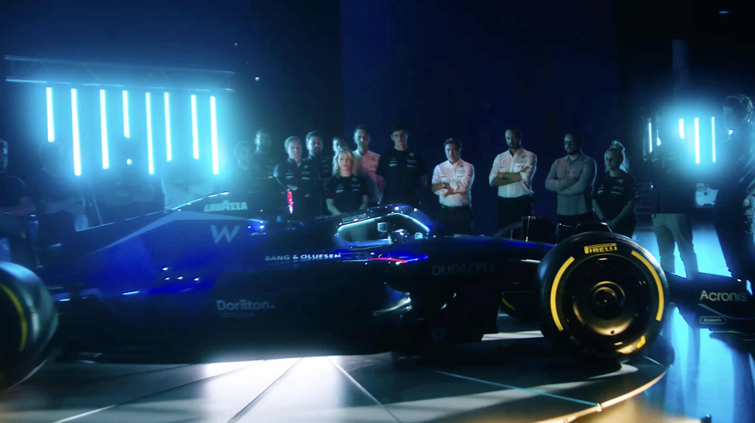 Team lined up behind the new Williams Racing F1 car under blue light columns