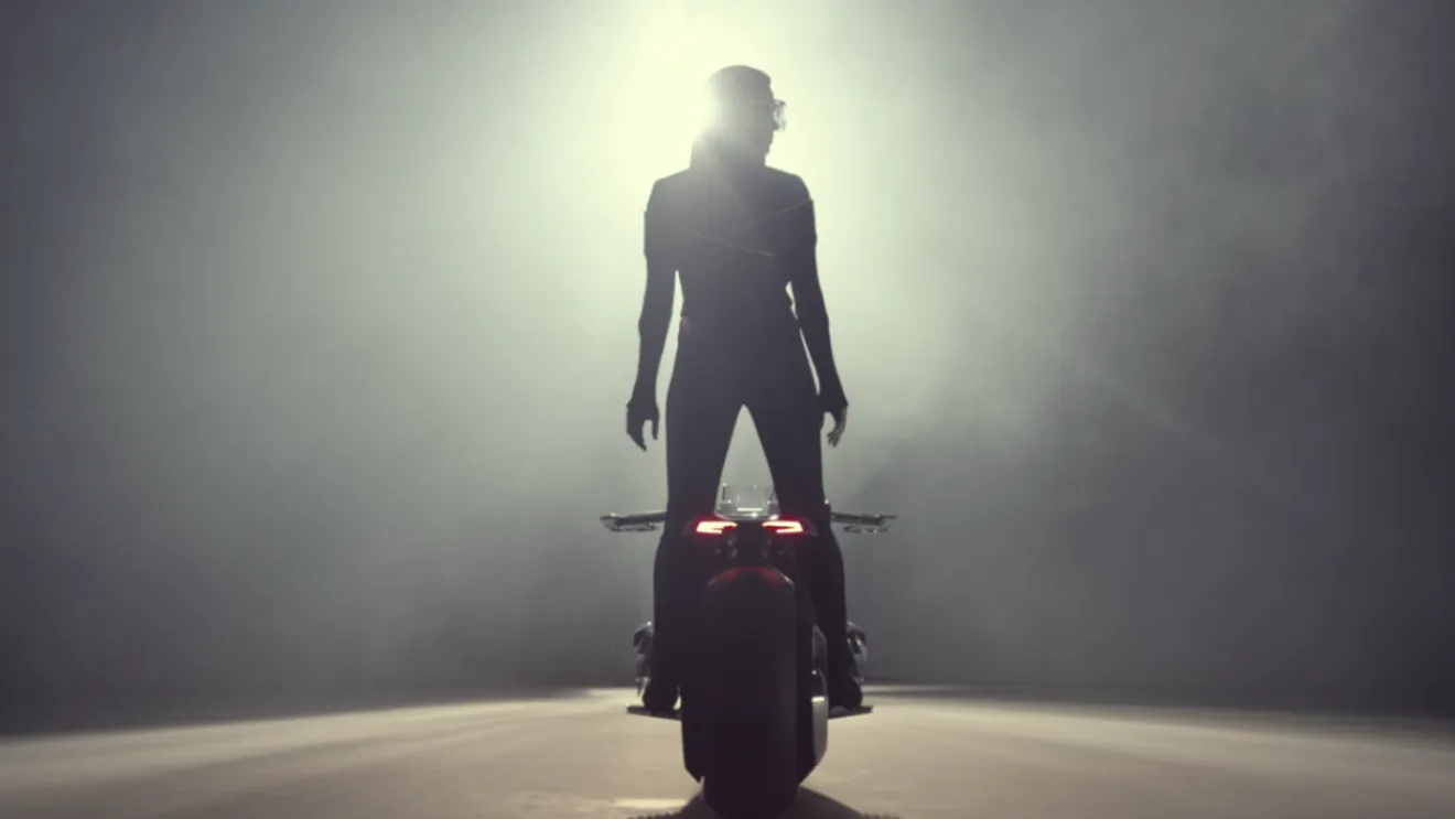 Rider standing on the BMW Motorrad VISION NEXT 100 in fog, lit from behind