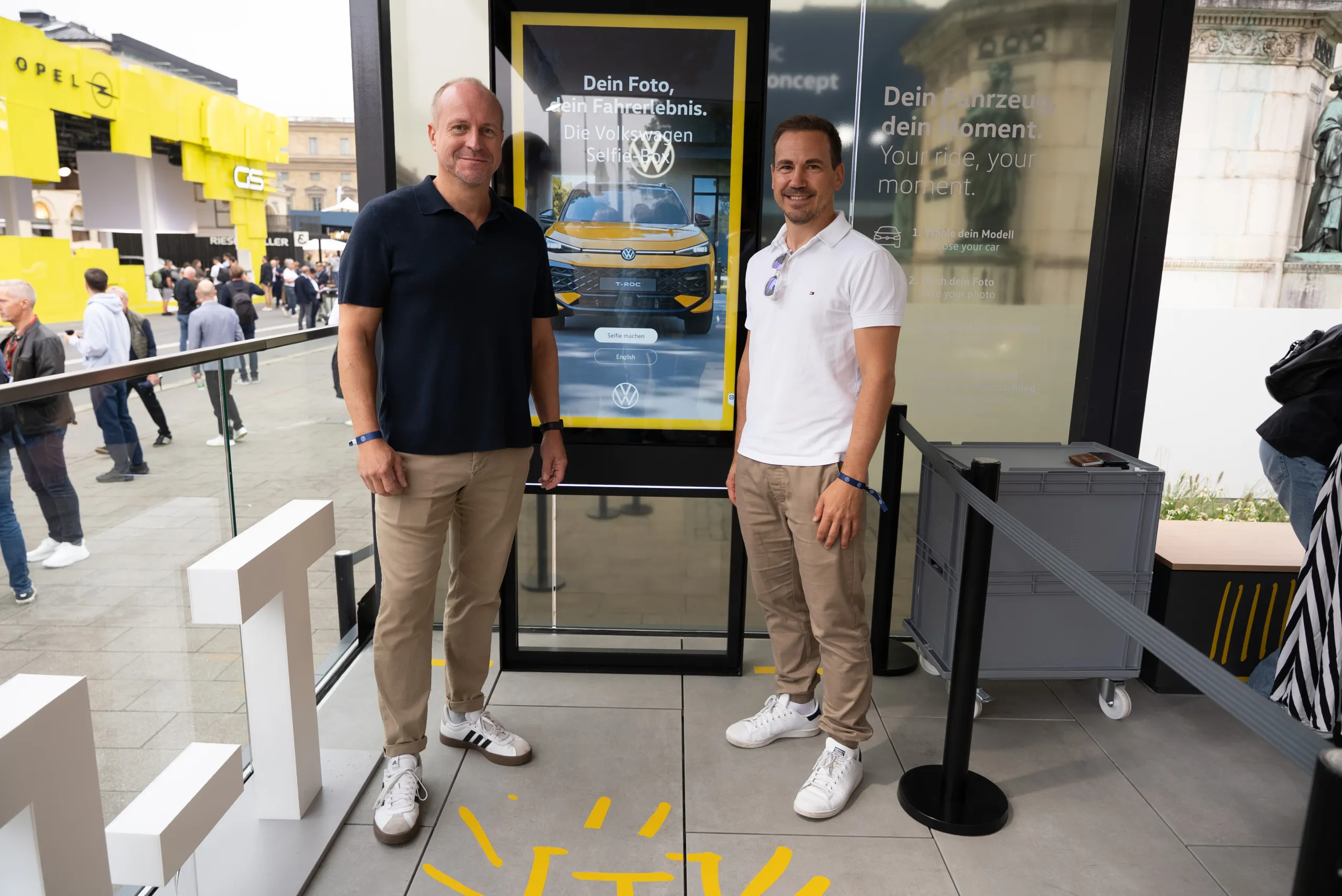 Two men posing in front of the Volkswagen Selfie Box screen at IAA MOBILITY 2025